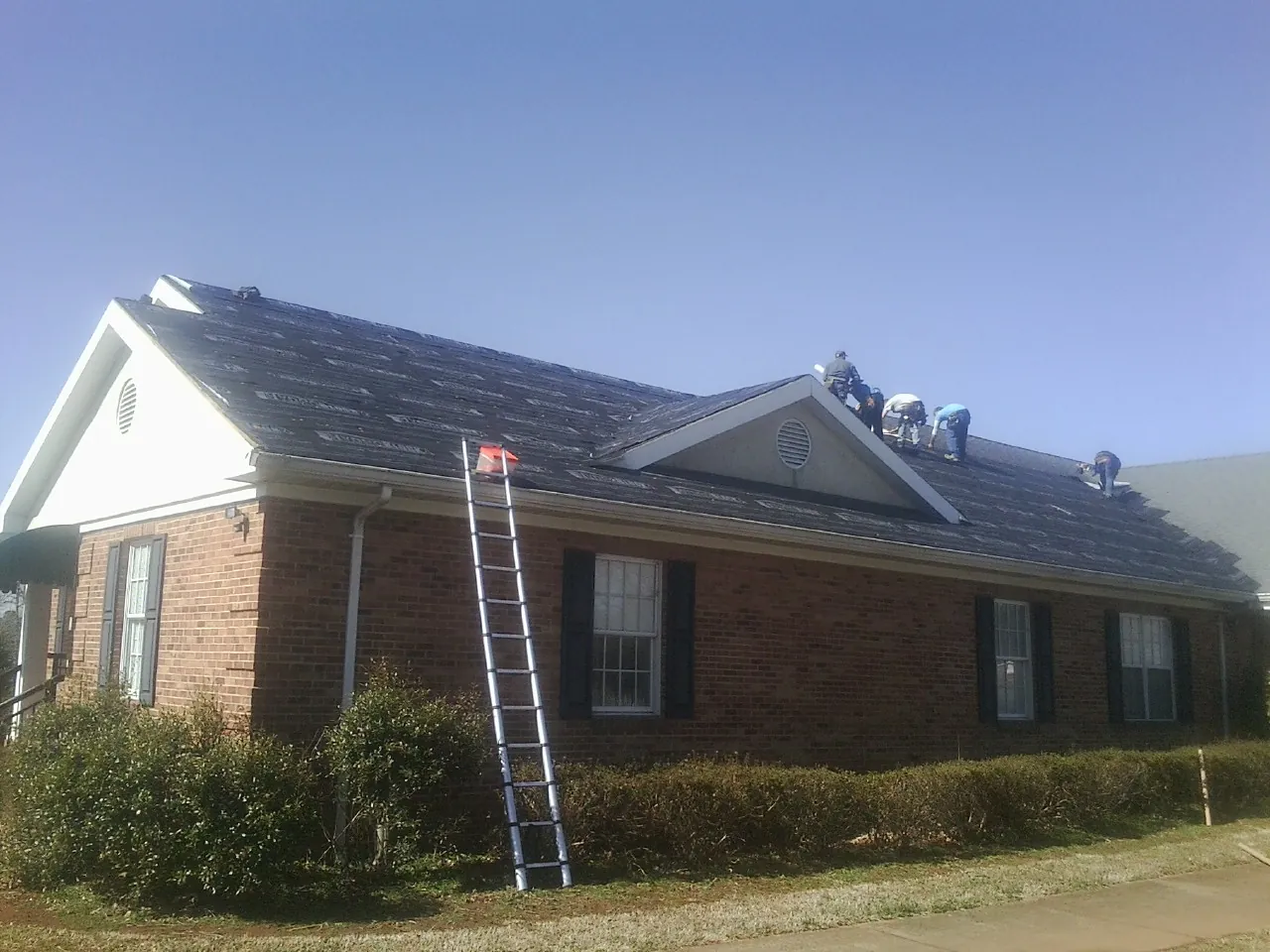 Crew tearing shingles off a brick ranch roof with a ladder set — Metal Roof Repair work by our crew in Inchelium