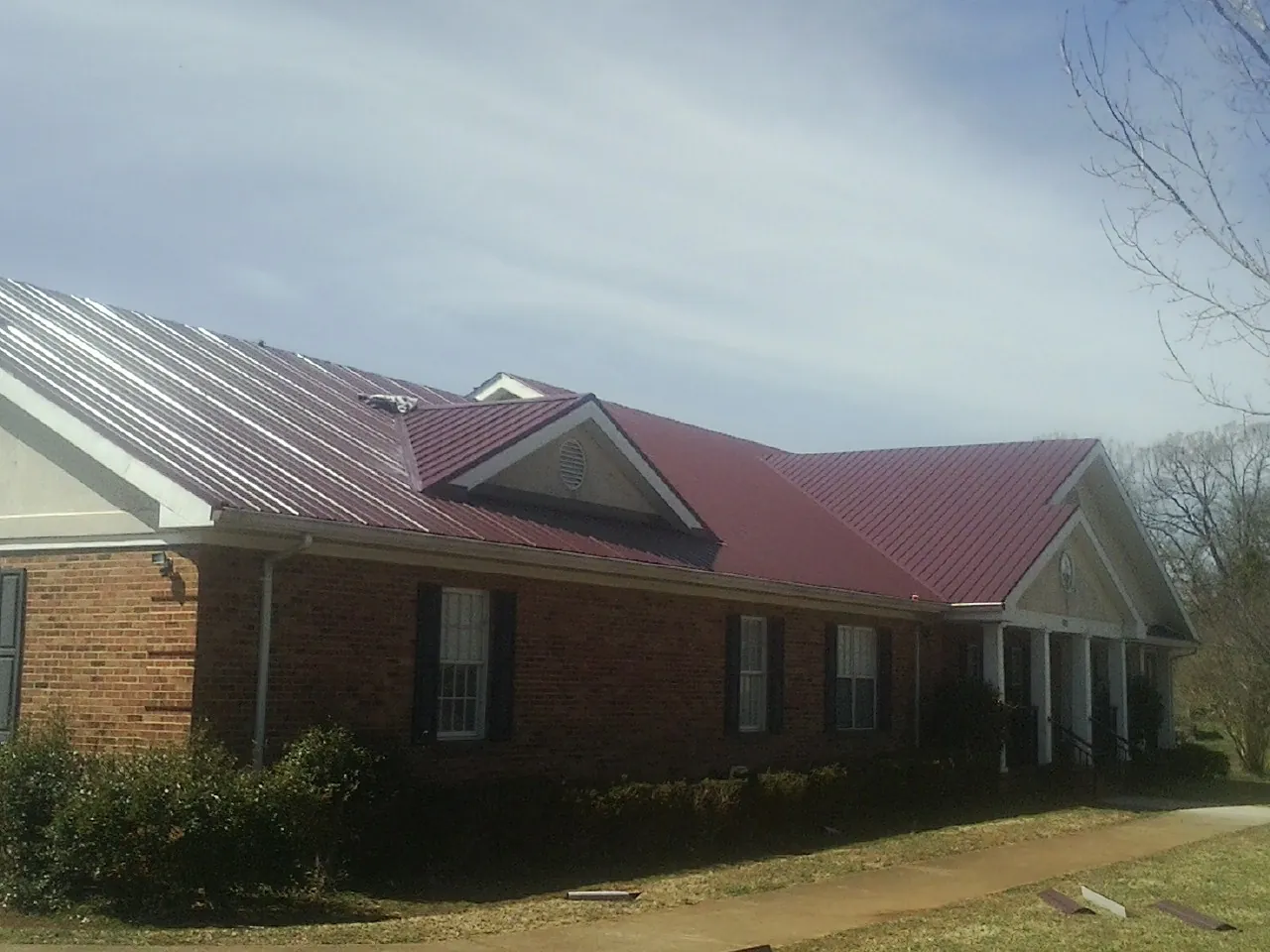Red metal roof with gabled entries on a long brick building, from a Hail Damage Roof Repair job in Inchelium