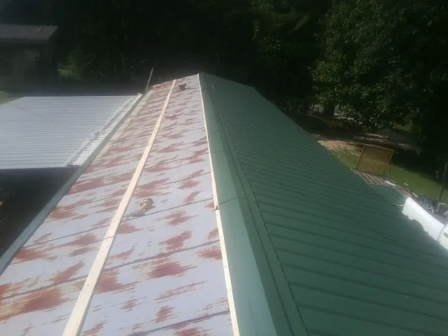 Old rusted panels beside newly installed green metal roofing — Wind Damage Roof Repair by Roofing Brothers in Inchelium