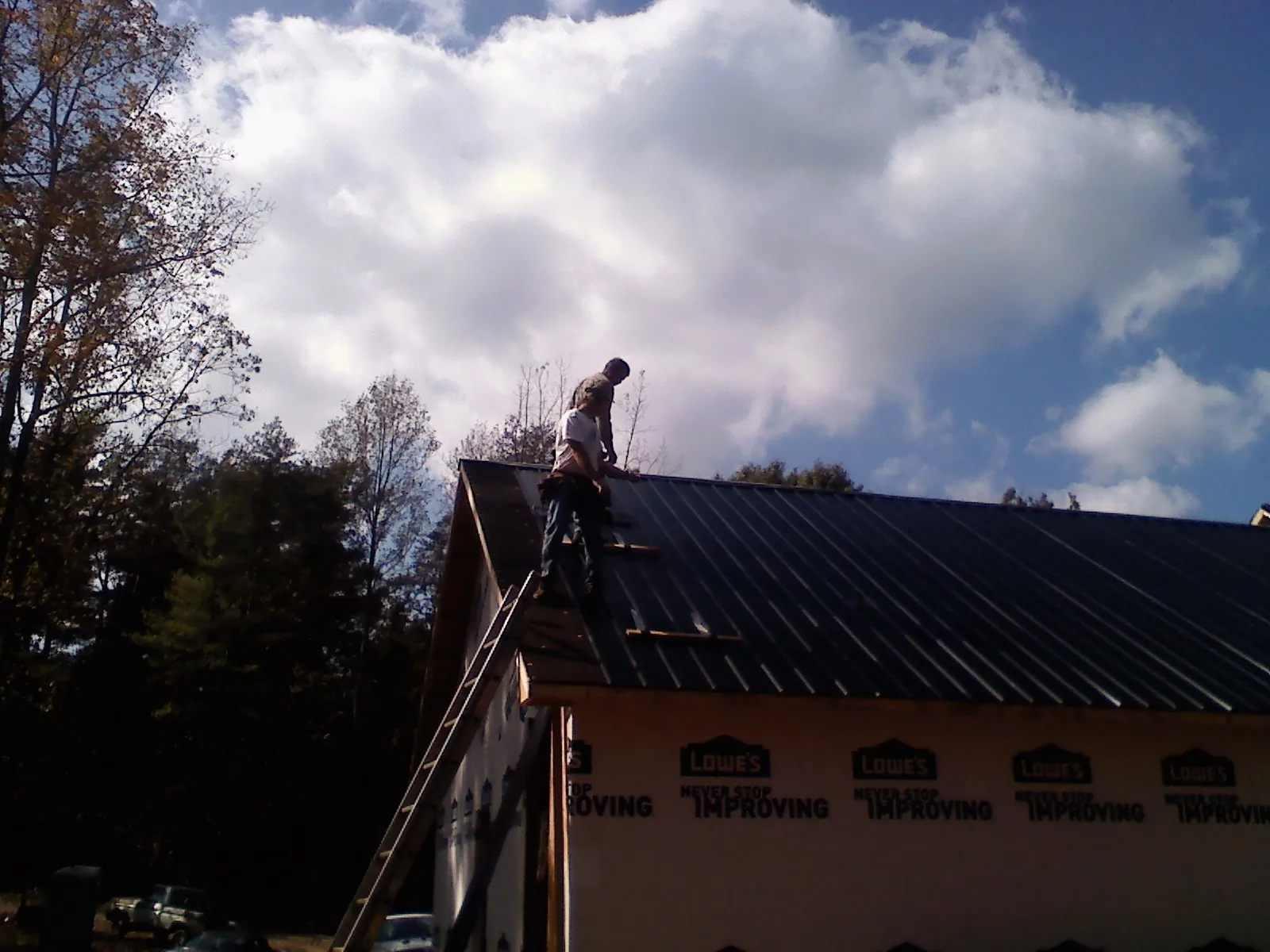 Roofer fastening dark metal panels high against a cloudy sky, from a Roof Inspection job in Inchelium