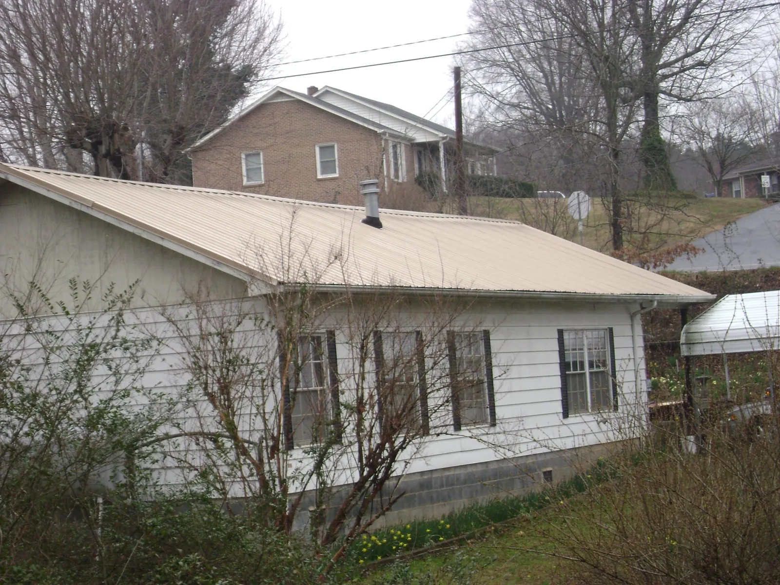 Tan metal roof on a white sided house set into a hillside — Commercial Roofing by Roofing Brothers in Inchelium