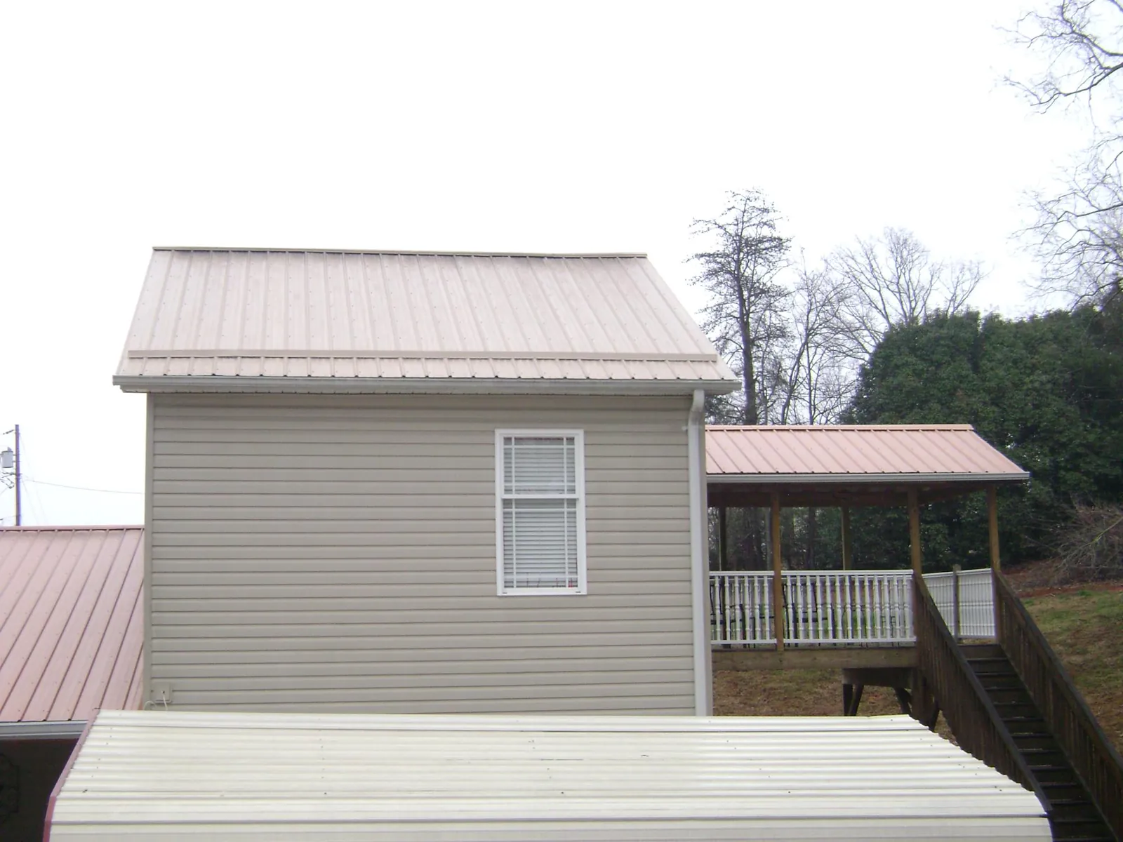 Tan metal roofs on a two story addition and attached porch, from a Roof Replacement job in Inchelium